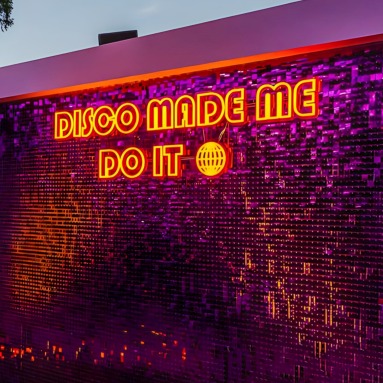 Disco Made Me Do It orange Custom Neon® sign on a shimmer wall outdoors @ultimo_catering