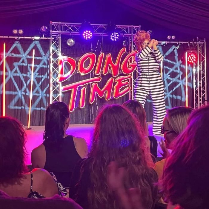 Performer on stage beside a red Custom Neon® 'Doing Time' backdrop sign under purple lighting