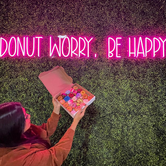 Pink Custom Neon® bakery quote sign on a green wall @getminidonuts