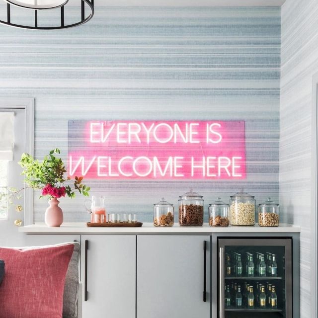 Red Everyone Is Welcome Here LED neon sign above a home snack and drinks bar