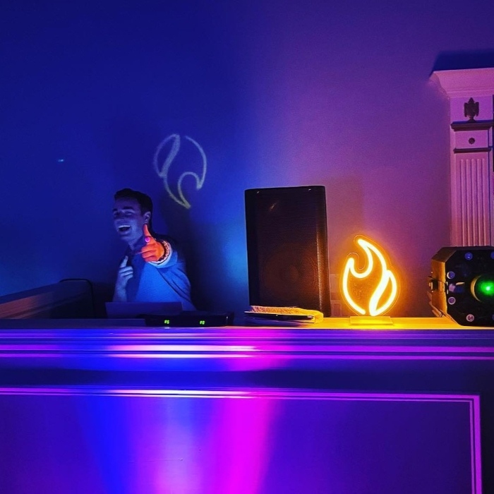 DJ giving a thumbs up in a blue-lit room beside an orange flame-shaped custom neon light