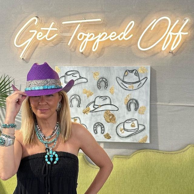 Woman in a purple cowboy hat posing under a warm white Get Topped Off script LED neon sign