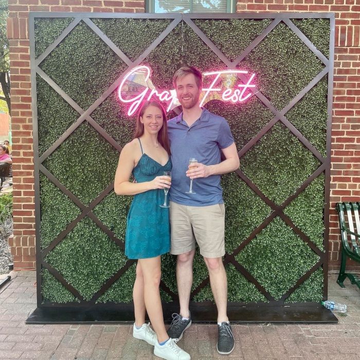 Smiling couple toasting under the pink GrapeFest custom LED neon sign at the Grapevine festival photo wall