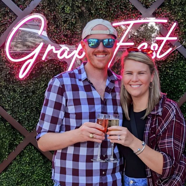 Couple taking a photo at a pink Custom Neon® 'Grape Fest' selfie wall in Texas