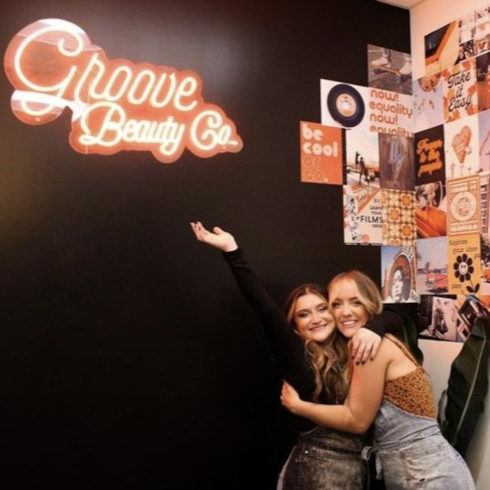 Orange Custom Neon® Groove Beauty Co logo on a dark wall in the @groovebeautyco salon