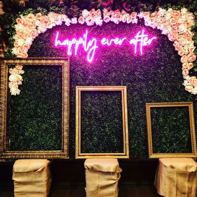 Happily Ever After pink Custom Neon® sign above 3 empty photo frames making up a wedding photo booth