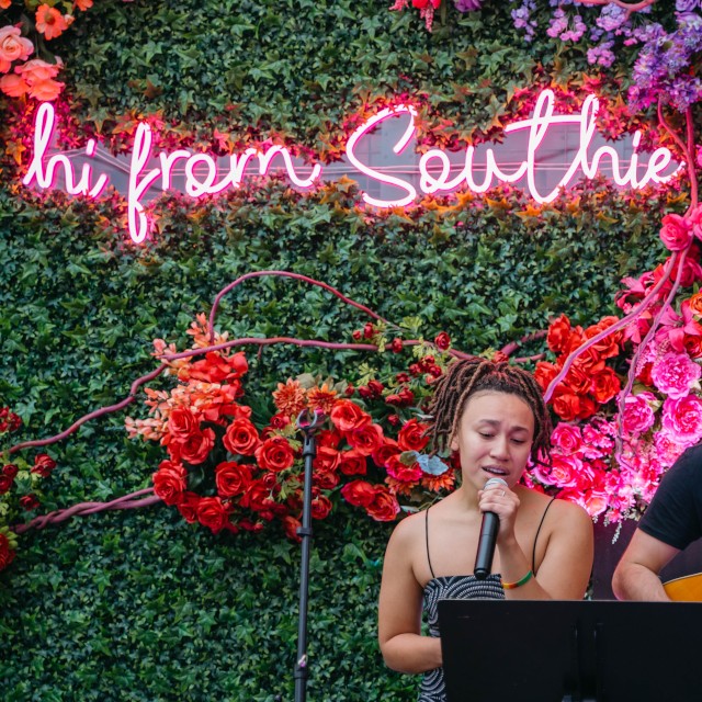 Hi From Southie hot pink Custom Neon® sign on large grasswall surrounded by florals @cannonballcafebos