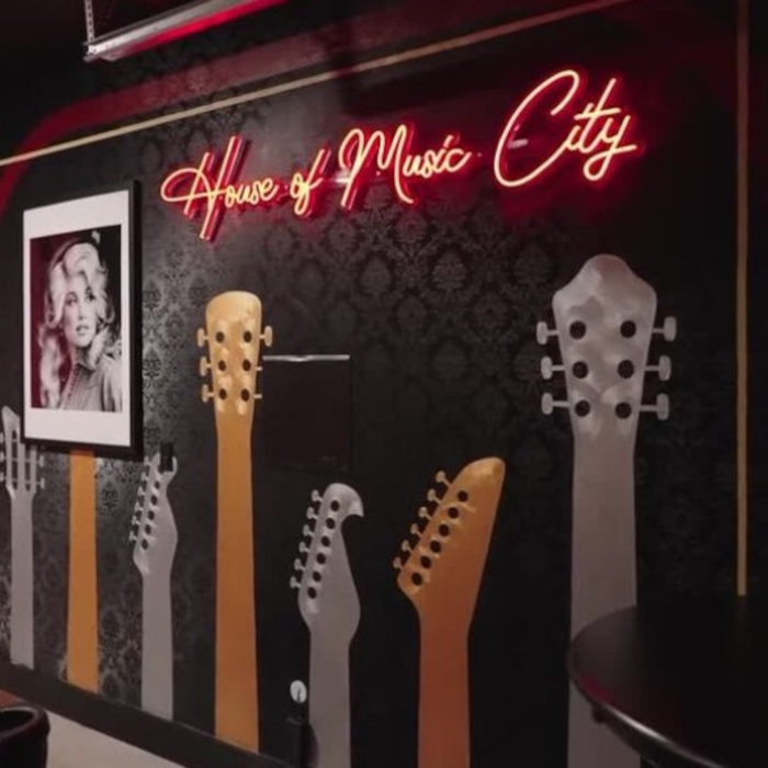 House of Music City red Custom Neon® sign on dark mural wall painted with guitars next to a photograph of Dolly Parton in an Airbnb designed by Somerled