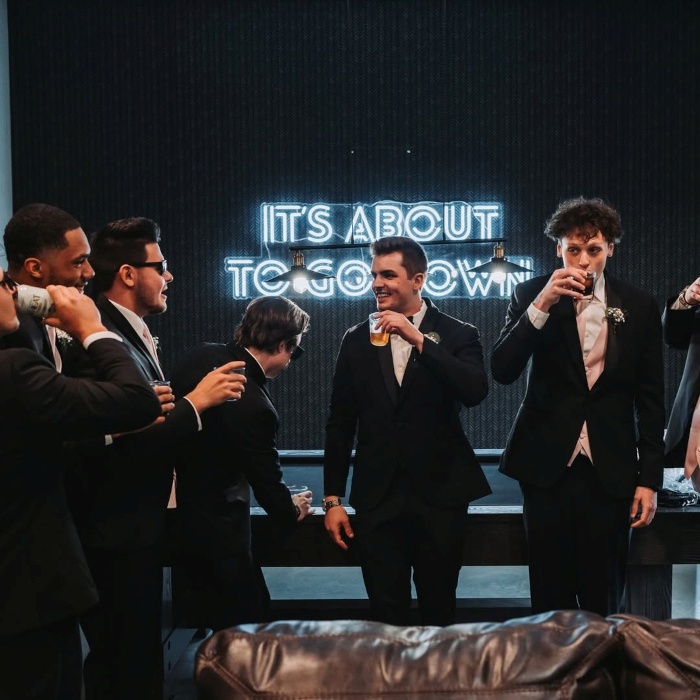 It's About to Go Down white Custom Neon® sign on a black wall in the groom's party room at @thehavenkc wedding venue