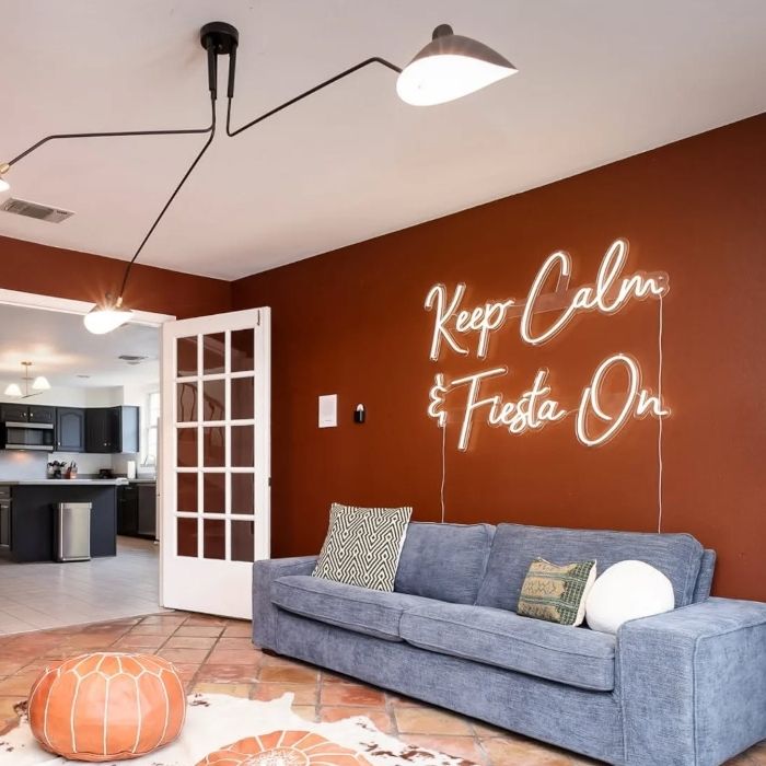 Keep Calm and Fiesta On warm white script LED neon sign on a terracotta wall above a blue sofa in a San Antonio living room