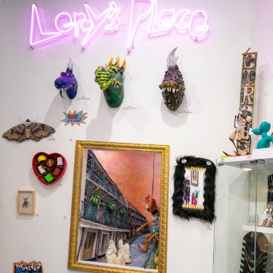 Pink 'Lenny's Place' sign above a display of quirky monster sculptures and eclectic framed artwork on a gallery wall