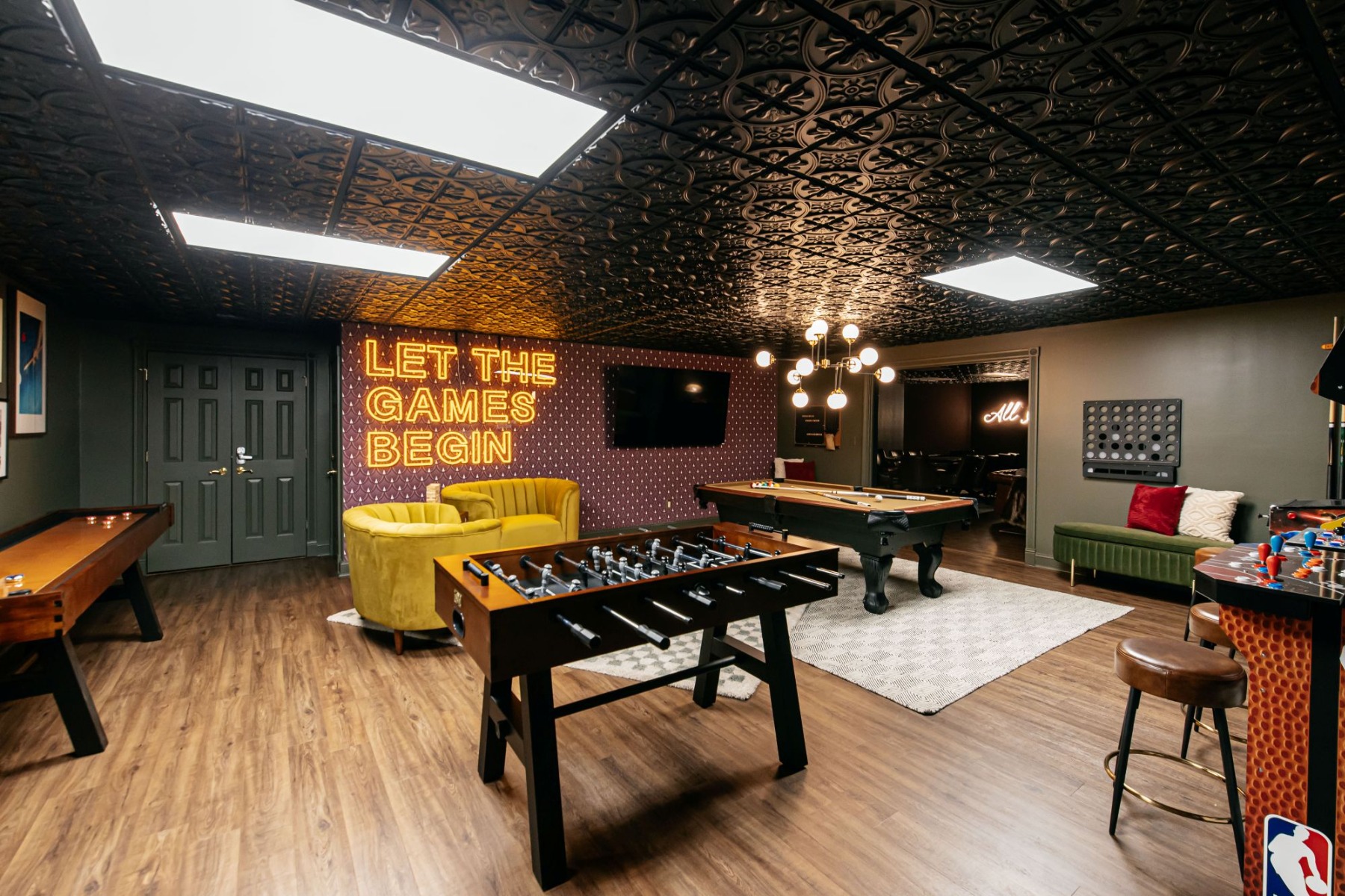 Let the Games Begin large dark yellow on a dark wall Custom Neon® sign in the games room of an Airbnb home designed by Somerled