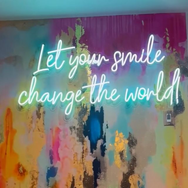 Mint green custom LED neon 'Let your smile change the world!' sign on a colorful abstract painted wall