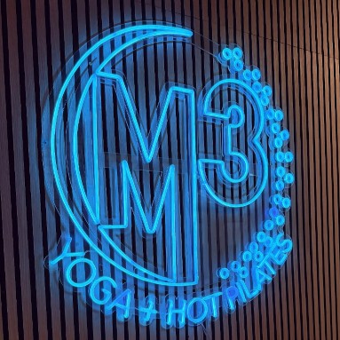 M3 Yoga and Hot Pilates circular logo in blue LED neon on a timber slat wall at their Atlanta studio