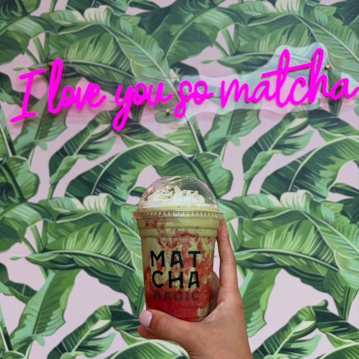 matcha drinkHand holding a Matcha Magic drink in front of a pink custom neon 'I love you so matcha' sign on a banana-leaf wall