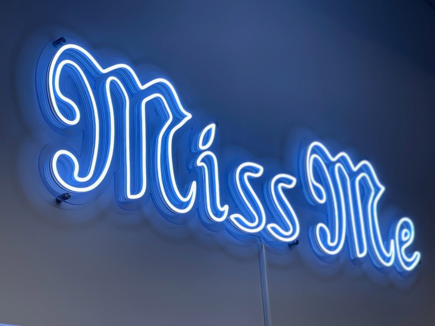 Blue Miss Me script LED neon sign with a layered acrylic backing on a studio wall
