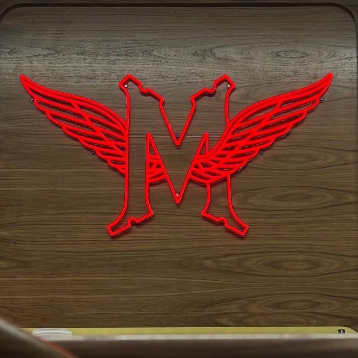 Red custom neon winged 'M' monogram sign mounted on a wood-panel wall