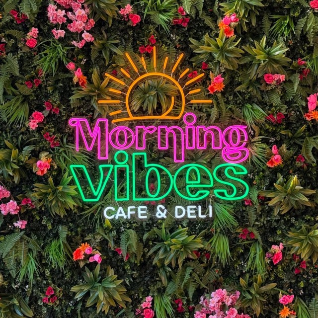 Morning Vibes Cafe and Deli colorful Custom Neon® logo sign on a lush plant wall