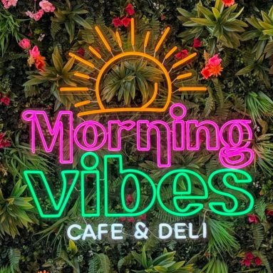 Morning Vibes Cafe and Deli colorful Custom Neon® logo sign on a lush plant wall