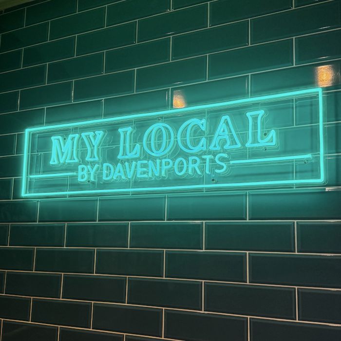 Mint green custom LED neon 'My Local by Davenports' sign mounted on a dark green metro-tiled wall