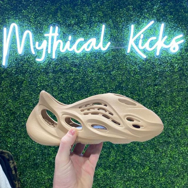 Custom Neon® footware store name sign on a grasswall with a shoe in the foreground @mythical.kicks