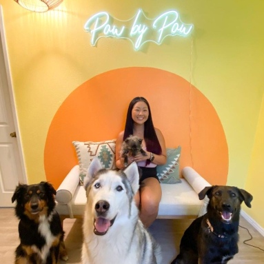 Custom Neon® white Paw by Paw sign on a yellow and orange mural wall for a dog training business