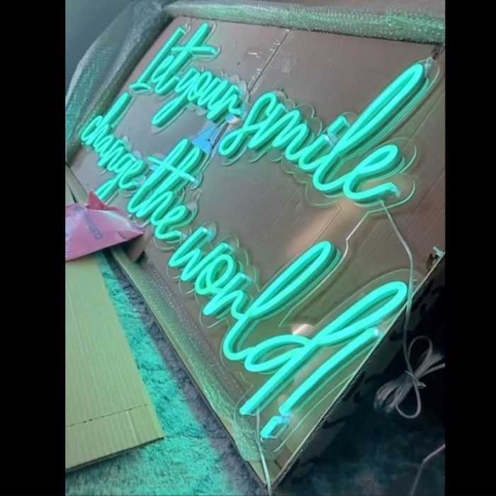 Mint green custom LED neon 'Let your smile change the world!' sign in a cardboard box with packaging