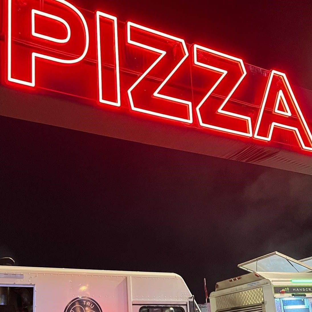 Red Custom Neon® 'Pizza' sign glowing on a festival food truck at night