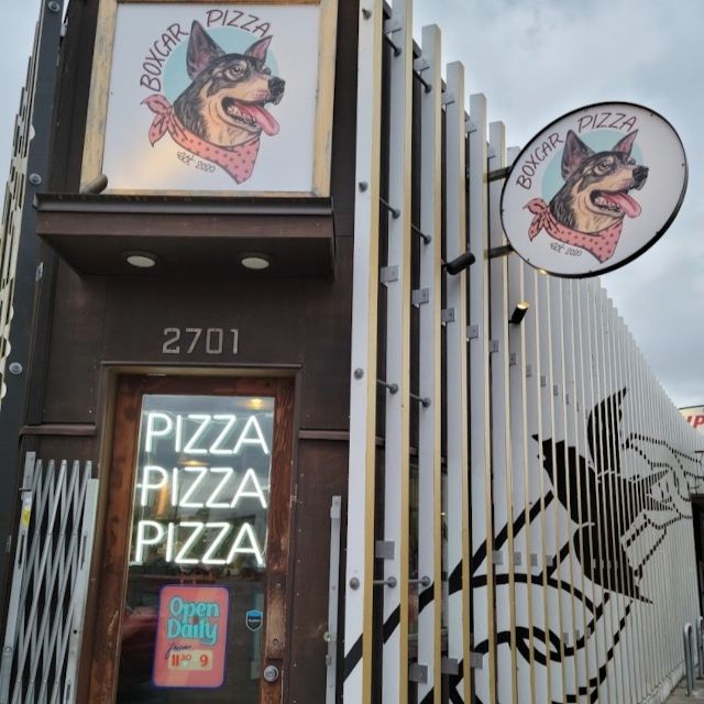 Boxcar Pizza storefront with a blue heeler dog logo sign and white custom neon 'Pizza Pizza Pizza' in the door window