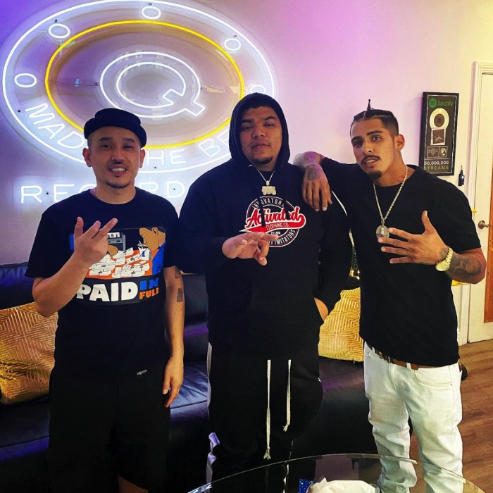 Large circular @qmadethebeat logo sign made by Custom Neon® on the wall behind the Q Made the Beat recording studio team