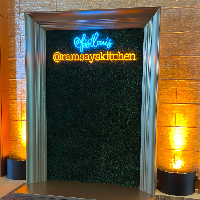 Custom Neon® blue and orange sign in a framed selfie station reading @fsstlouis @ramsaykitchen