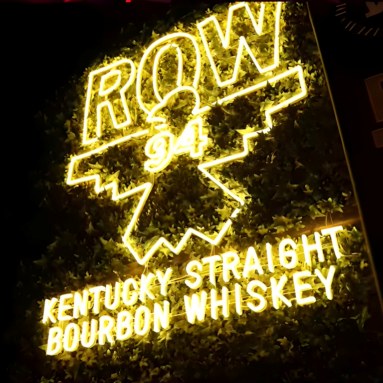 Warm white Custom Neon® sign featuring Row 94 Kentucky Straight Bourbon Whiskey on a dark wall 