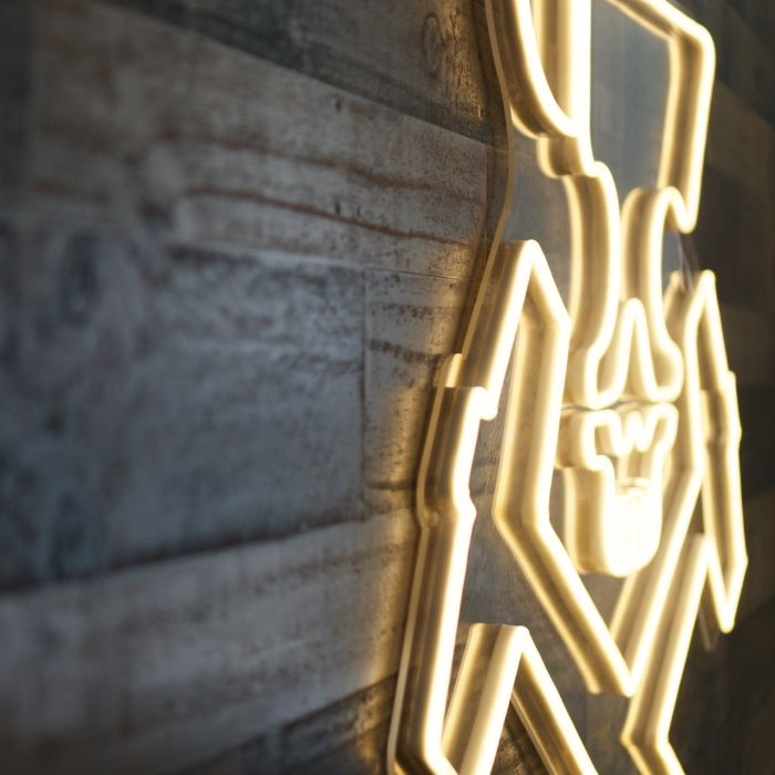 Close-up of the Rust Iron Gym logo glowing in warm white LED neon on a rustic timber feature wall