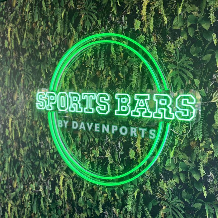 Green custom LED neon 'Sports Bars by Davenports' sign in a circular frame on a green foliage wall