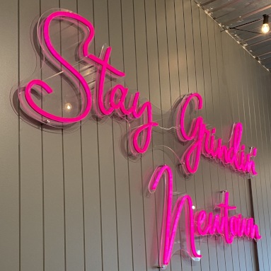 Hot pink Custom Neon® sign in a script font on a wood paneled wall in @blankspace_newtown