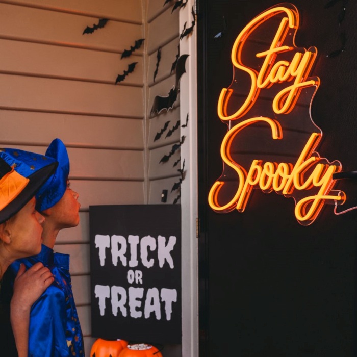 Orange Custom Neon® Stay Spooky sign a black door surrounded by Halloween decorations