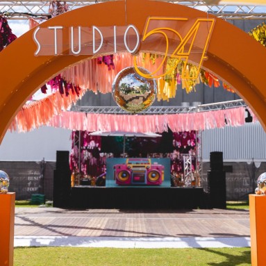 Disco Made Me Do It orange Custom Neon® sign on a purple shimmer wall at an outdoor disco party @ultimo_catering