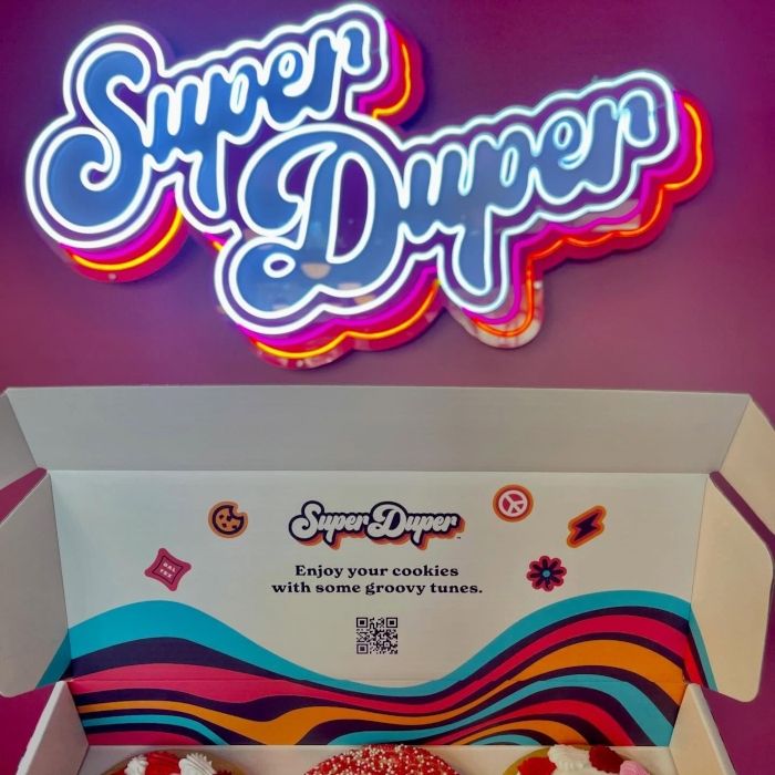 Super Duper Cookie Co retro script LED neon sign with layered pink, orange and yellow backing above an open cookie box