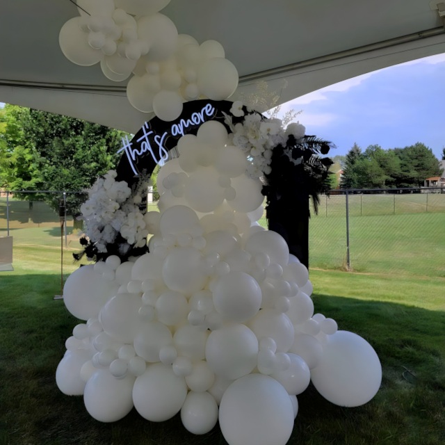 Custom Neon® white That's Amore sign on a greenwall behind a wooden swing surrounded by a yellow and green balloon arch - event decor by @decorandfiesta