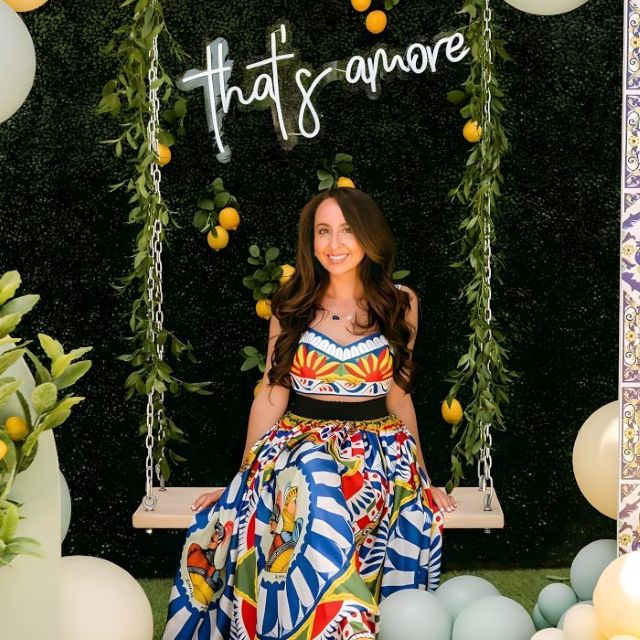 Custom Neon® white That's Amore sign on a greenwall behind a wooden swing surrounded by a yellow and green balloon arch - event decor by @decorandfiesta