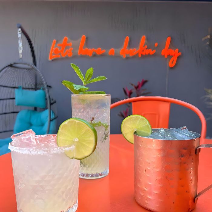 Cocktails on a table in front of an orange neon sign at The Blue Duck in New London CT