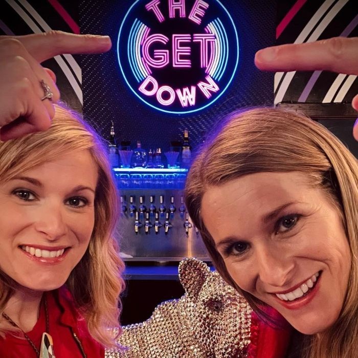 Down sign	Two women taking a selfie pointing up at a purple, pink and blue custom neon 'The Get Down' record logo sign above a bar