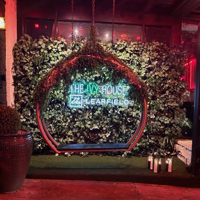 The Ivy House and Learfield green LED neon sign set into a greenery wall behind a hanging swing seat