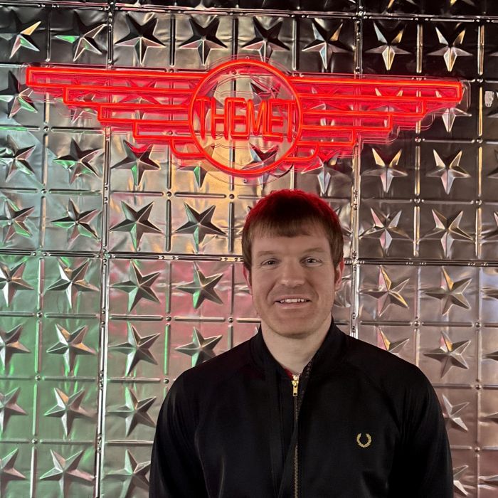 Man standing in front of a custom red LED neon 'The Met' winged logo sign on a silver star-embossed tile wall in a Davenports sports bar