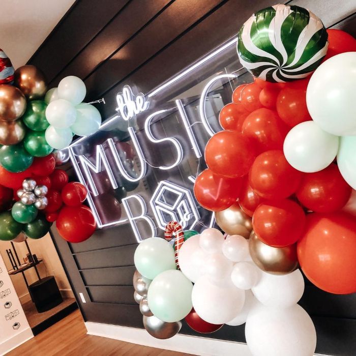White custom neon 'the Music Box' sign framed by a red, green, gold and white Christmas balloon garland