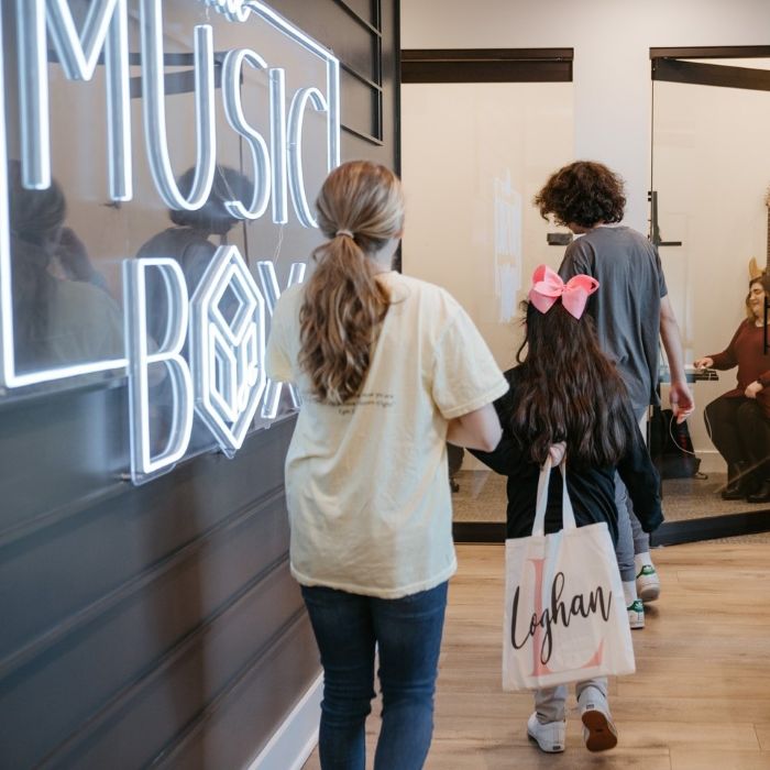 Family walking into a music school lobby past a large white custom neon 'the Music Box' sign