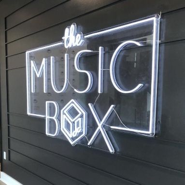 White custom LED neon the Music Box sign mounted on a dark shiplap wall