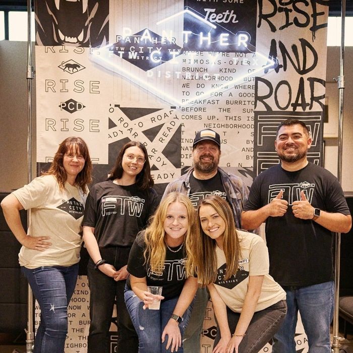 Panther City District team posing in front of their custom LED neon sign in Fort Worth