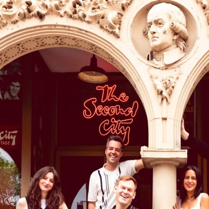 The Second City Custom Neon® sign under a carved stone archway with four guests posing in Old Town