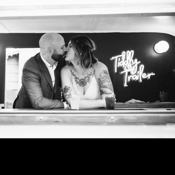 Newleyweds kissing inside the Tiddly Trailer bar van with a white Custom Neon® white sign in the background
